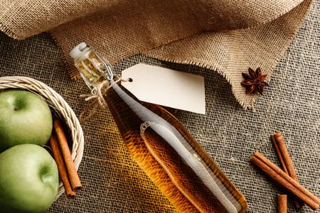 Composition with a bottle of apple juice or cider, a basket with apples and cinnamon sticks on a burlap. The concept of home-made products.の写真素材
