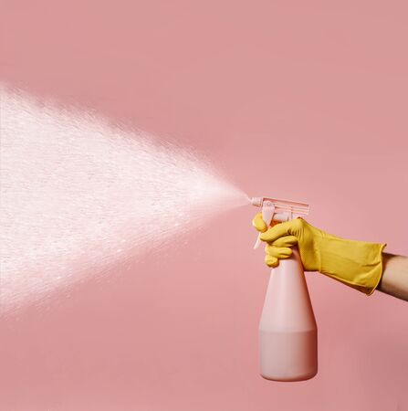 A hand in a silicone household glove holds a liquid spray bottle on a pink background with space for text.. A stream of water hits from the atomizer. The concept of maintaining cleanliness and order in the house.の写真素材