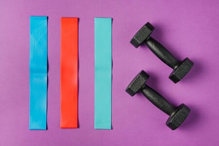Multi-colored elastic bands for fitness and two dumbbells on a colored background. Concept of home workout and sport lifestyle.の写真素材