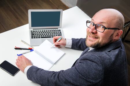 A businessman with glasses works with papers and a laptop, turning to the camera over his shoulder.の写真素材