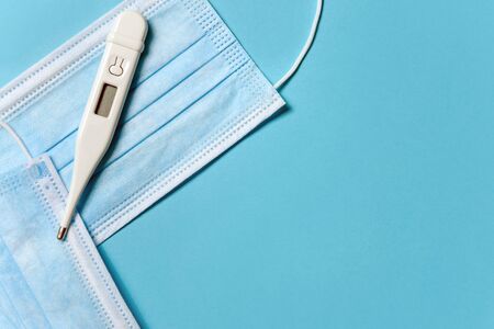 Medical masks and thermometer on a blue background with space for text. The concept of modern...