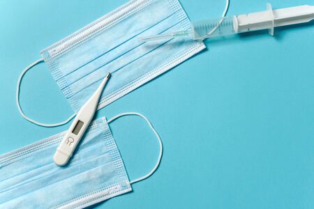 Medical masks, thermometer and syringe on a blue background. Health Protection Concept with place...