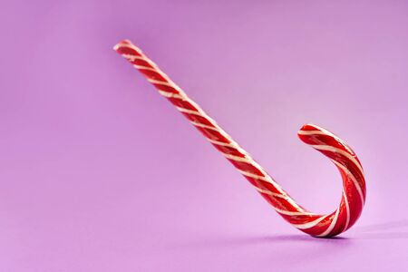 Striped red and white lollipop on a purple background with space for text.の写真素材