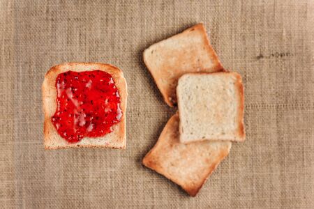 Bread toast smeared with raspberry jam levitates against the background with three toasts lying on a burlap. Breakfast concept with selective focus.の写真素材
