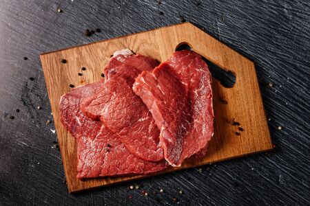 Three juicy slices of beef for steaks on a cutting board. Flat lay composition with raw meat and...