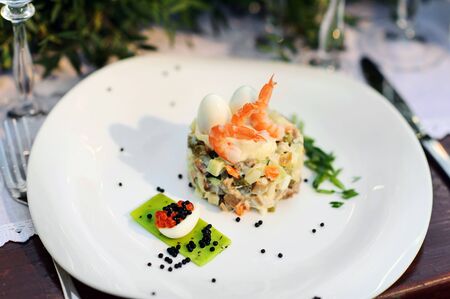 Salad with shrimp, quail eggs, red and black caviar on a dish.