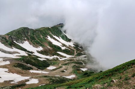 Mountain landscape with cloud and fog. Road and a small lake high in the mountains in cloudy weather.の写真素材