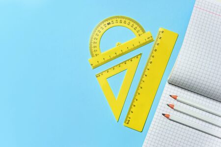 Squared school notebook, pencils and set of rulers on a blue background with copy space. The concept...