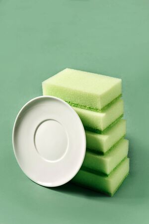 Several sponges for washing dishes and a white saucer on a green background. The concept of home care and housekeeping.の写真素材