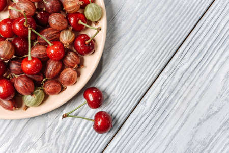 Plate with cherries and gooseberries on a wooden background with copy space. Summer Harvest Concept.の写真素材