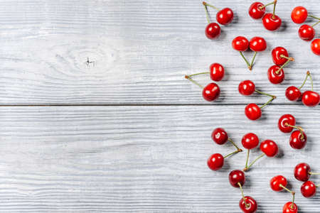 Ripe cherries lie on the edge of a table of light rough planks with a copy space.の写真素材