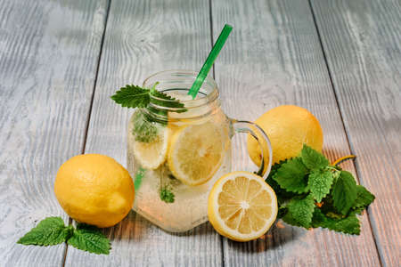 Lemonade in a glass with lemon, and mint leaves. Refreshing soft drink in a glass on a wooden table...