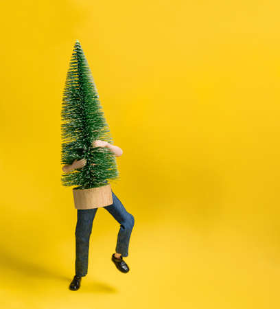 The doll carries a toy Christmas tree on a yellow background with copy space. Christmas and New Year preparation concept.の写真素材
