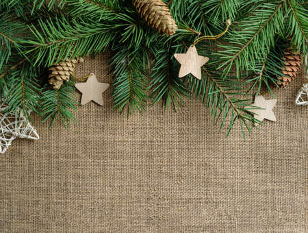Fir branches, decorated with wooden Christmas decorations, lie on a burlap background with copy space.の写真素材
