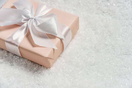 Gift box with a bow in the snow. Christmas festive gift on a light background with copy space.の写真素材