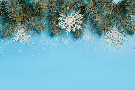 Fir branches with snowflakes and snow flakes on the edge of a blue background. Christmas frame with copy space.の写真素材