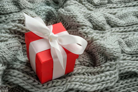 Gift box with a bow on a knitted plaid background. Christmas gift in a red box.の写真素材