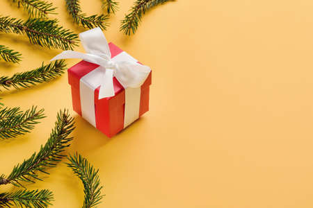 Gift box with a bow among the Christmas tree branches on a yellow background with copy space.の写真素材