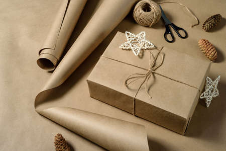 Gift wrapping in brown kraft paper. Gift box with craft paper, scissors, pine cones and a skein of twine.の写真素材