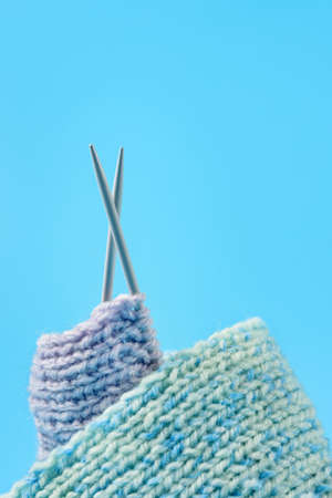 knitted scarf with knitting needles on a blue background.