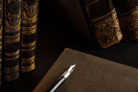 An antique fountain pen, shot close-up with selective focus on the background of old book spines. Writing craft.の写真素材