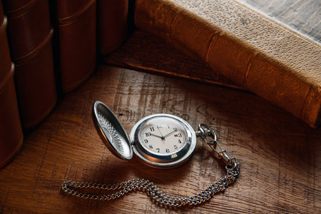 An old pocket watch with a chain lies on the table near vintage books.