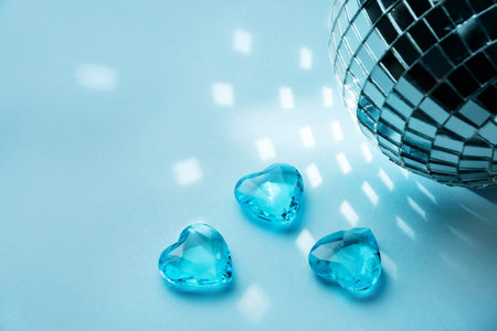 Three crystal hearts of blue on a blue background with a disco ball. Lovers' holiday concept.