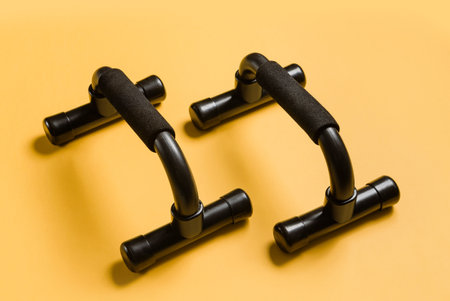 Black push up bars on a yellow background close-up. Home workout equipment.の写真素材