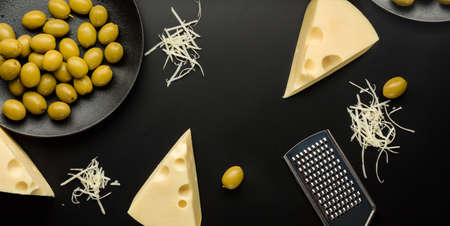 Flat lay composition with pieces of cheese and olives on a dark background.の写真素材