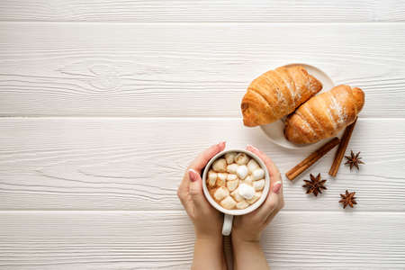 Flat lay composition with a mug of cocoa in female hands and croissants on a platter.の写真素材