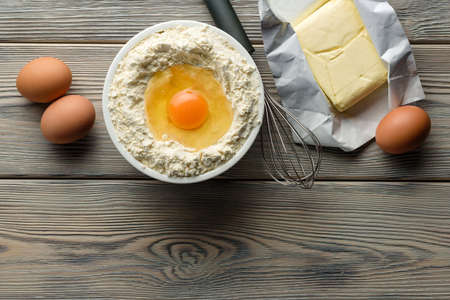 Flat lay composition with ingredients for making dough. Flour, eggs, whisk and butter on a wooden...