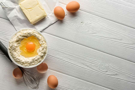 Ingredients for making dough on a white wooden table with copy space. Flour, eggs, butter and a...