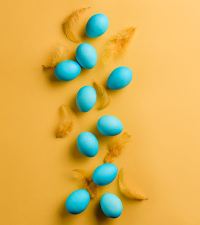 Blue Easter eggs and yellow feathers on a yellow background with copy space. Easter banner.の写真素材