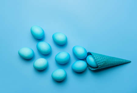 A composition with Easter eggs and a waffle cone in blue. Easter eggs scattered from an ice cream cone on a blue background.の写真素材