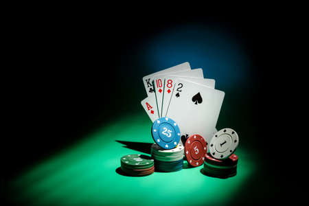 Poker cards and playing chips in a beam of light on a dark background with copy space. Gambling...