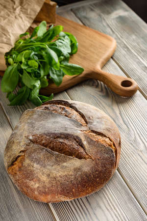 Homemade dark bread close-up on the table. Loaf of bread and spinach on a cutting board.