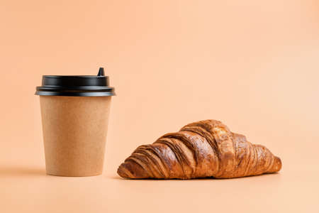 Croissant and disposable beverage glass on a cream colored background. Coffee and croissant.の写真素材