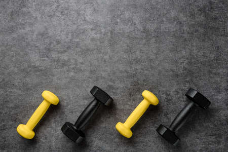 Black and yellow dumbbells on a dark textural background with copy space. Flat lay composition with dumbbells.の写真素材