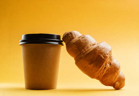 A glass of coffee and a croissant close-up on a yellow background.の写真素材