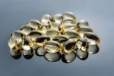 Vitamin D3 capsules close-up with selective focus and reflection on a smooth mirror surface.