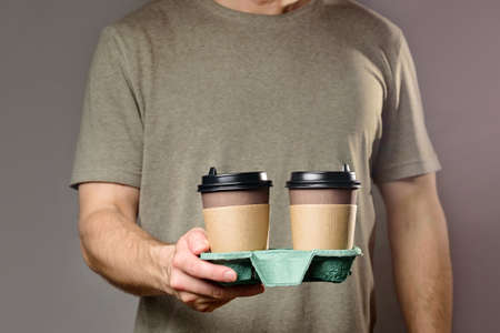A man holds a cardboard cup holder with two disposable coffee cups. Takeaway drinks.の写真素材