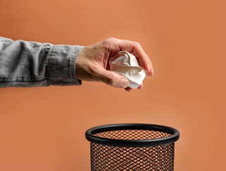 Man's hand throws crumpled paper into a basket on a beige background with copy space.の写真素材