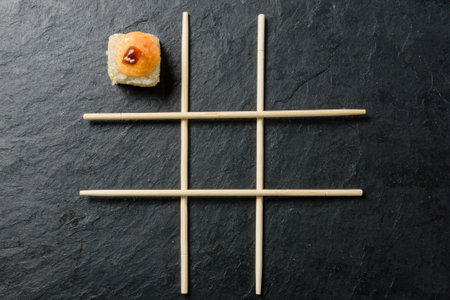 chopsticks arranged in a tic-tac-toe pattern and one roll on a dark stone background.の写真素材