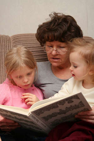 Grandmother sitting on the armchair with her grandchildren and reading