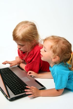 Two little girls playing on laptop on a light backgroundの写真素材