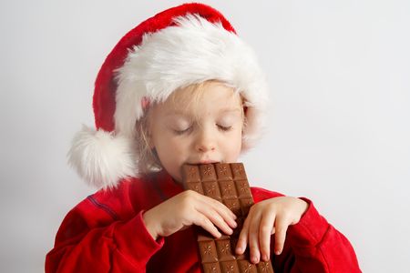 Little girl wearing red Santa hat eating chocolateの写真素材