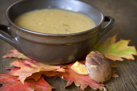 Mushroom soup and autumnal leaves on a brown tableの写真素材