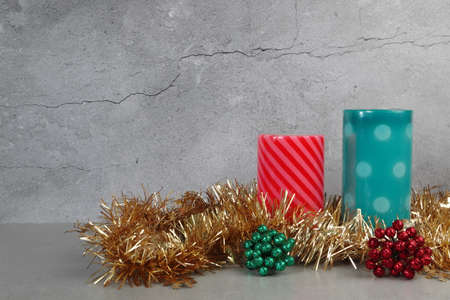 Christmas scent pillar red and green colours candles are on the grey table with Christmas glitter ornaments with background of cracking cement wallの写真素材