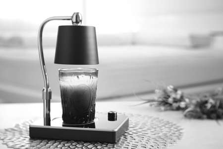 The luxury lighting aromatic scent  glass candle is put on the electric lamp candle warmer heater on the grey table in the white bedroomの写真素材