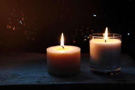 aromatic scent ivory colour pillar candle lighting on the wooden table with a small plant pot near the curtain in the dark bedroom in the summer morningの写真素材